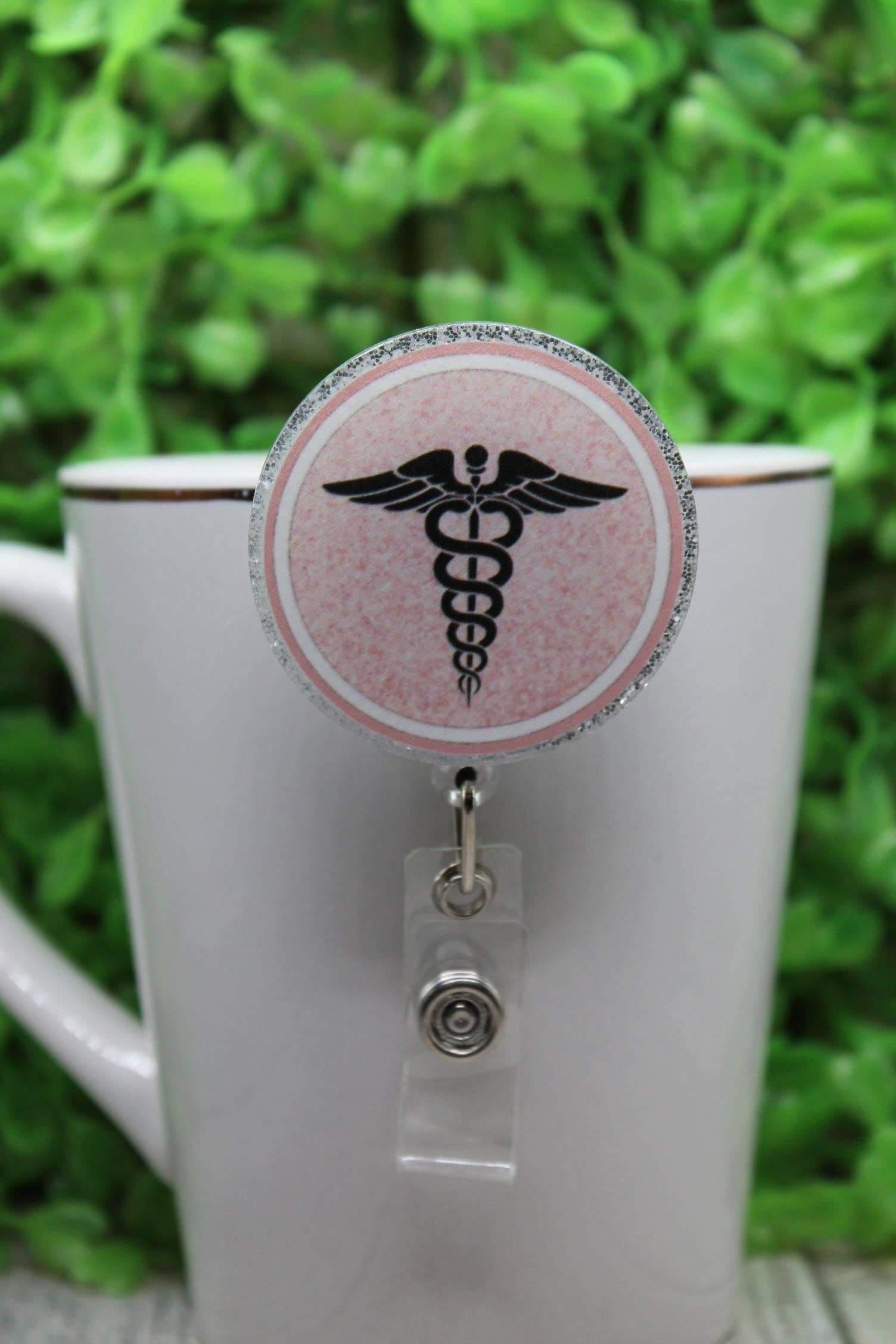 Circular badge reel with a pink nurse emblem, featuring a retractable clip, ideal for nursing uniforms.